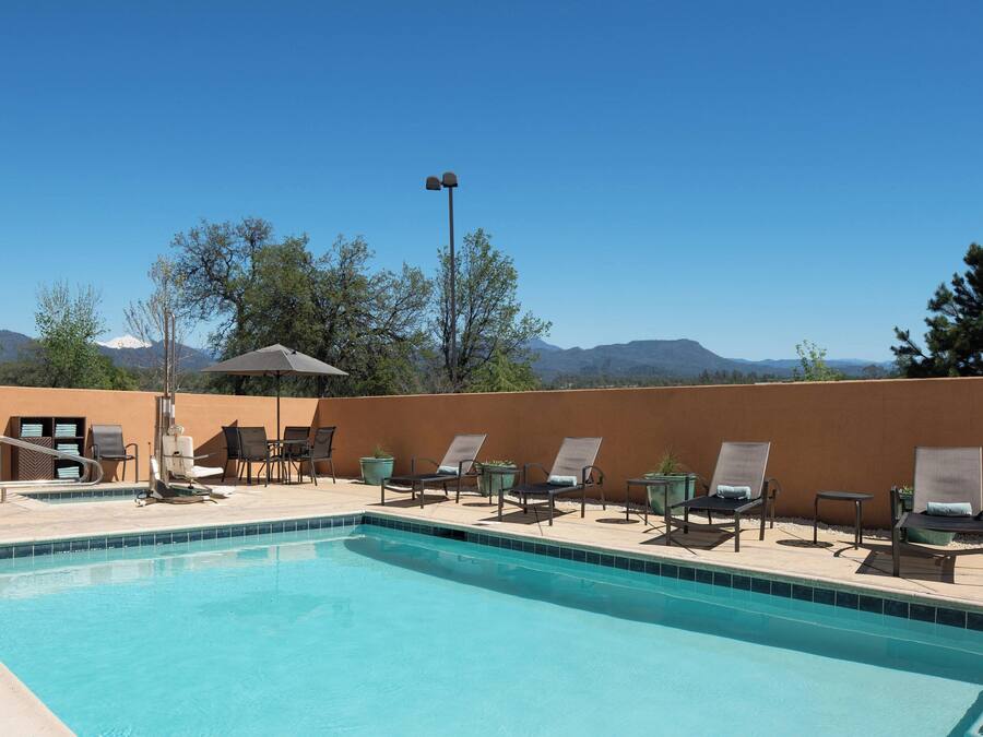 A pool area with lounge chairs and a table, surrounded by a low wall and trees.
