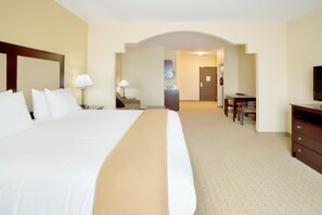 A hotel room with a large bed, a desk, a chair, a television, and a bathroom visible through an archway.