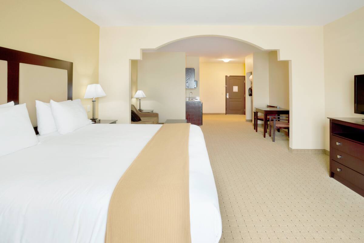 A hotel room with a large bed, a desk, a chair, a television, and a bathroom visible through an archway.