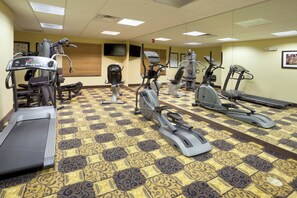 A gym with various cardio machines, a patterned floor, and a television on the wall.