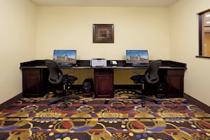 A hotel room with two desks, two chairs, a carpet with a geometric pattern, a framed picture on the wall, and a window.