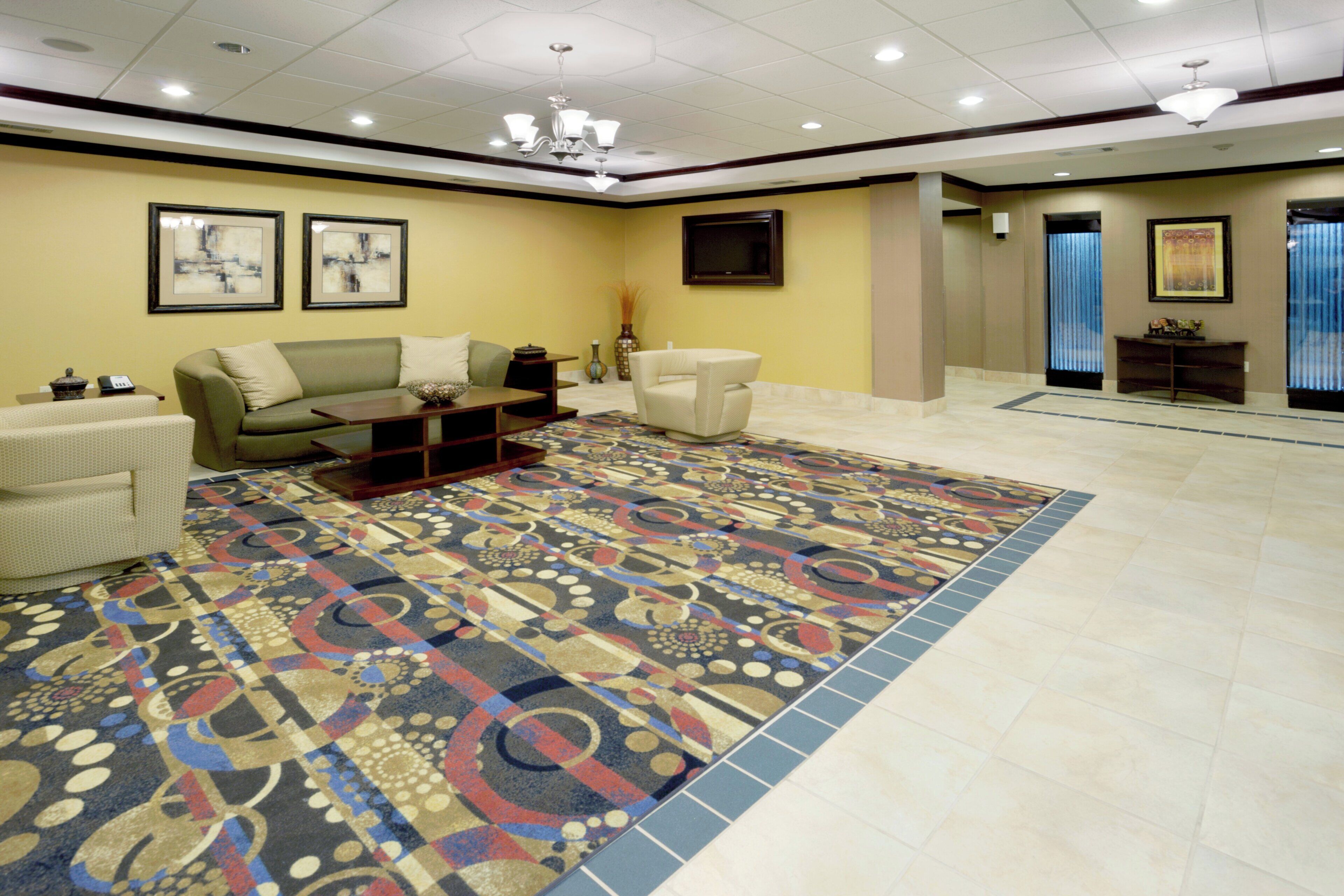 A hotel lobby with a patterned carpet, a sofa, a chair, and a small table.