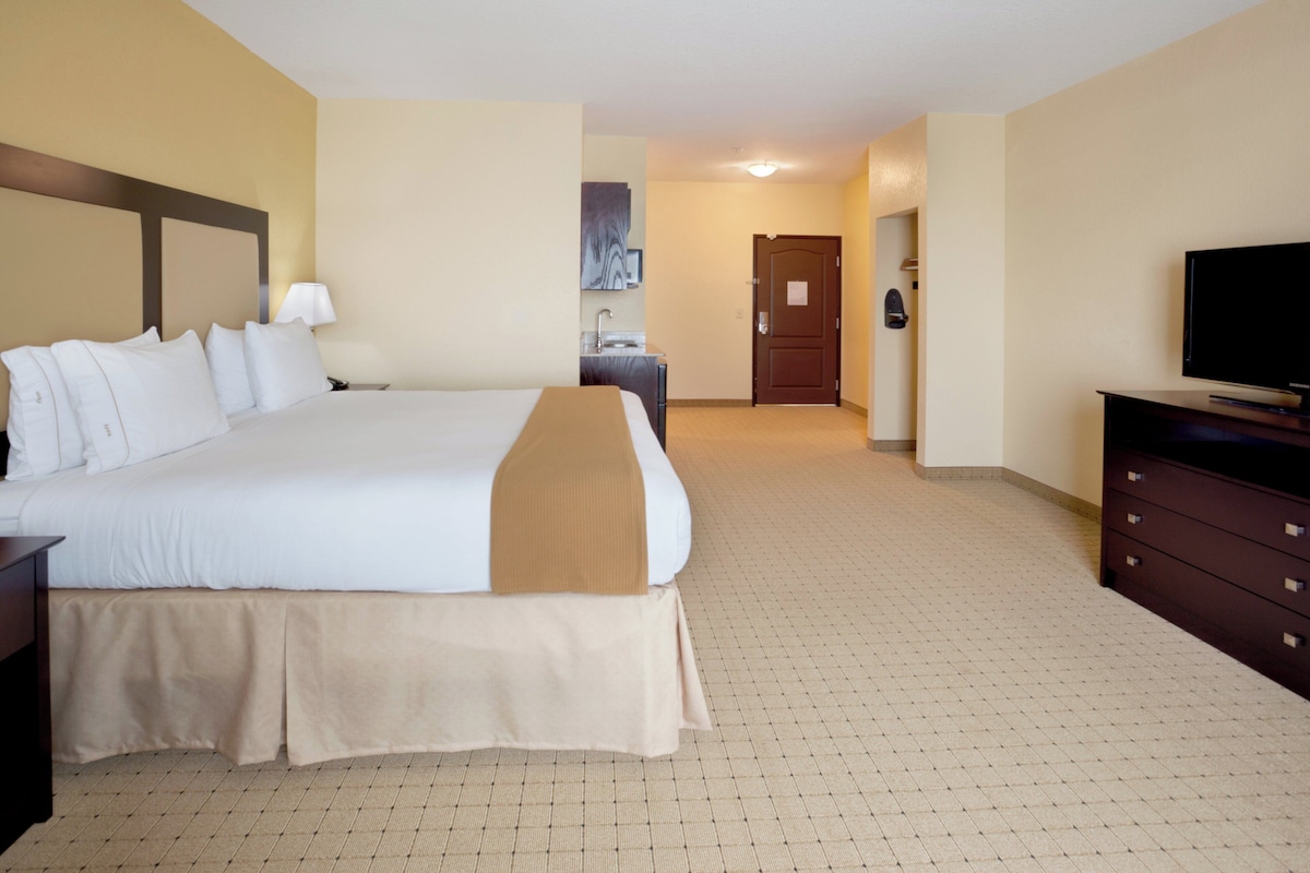 A hotel room with a large bed, a dresser, a television, and a bathroom visible in the background.