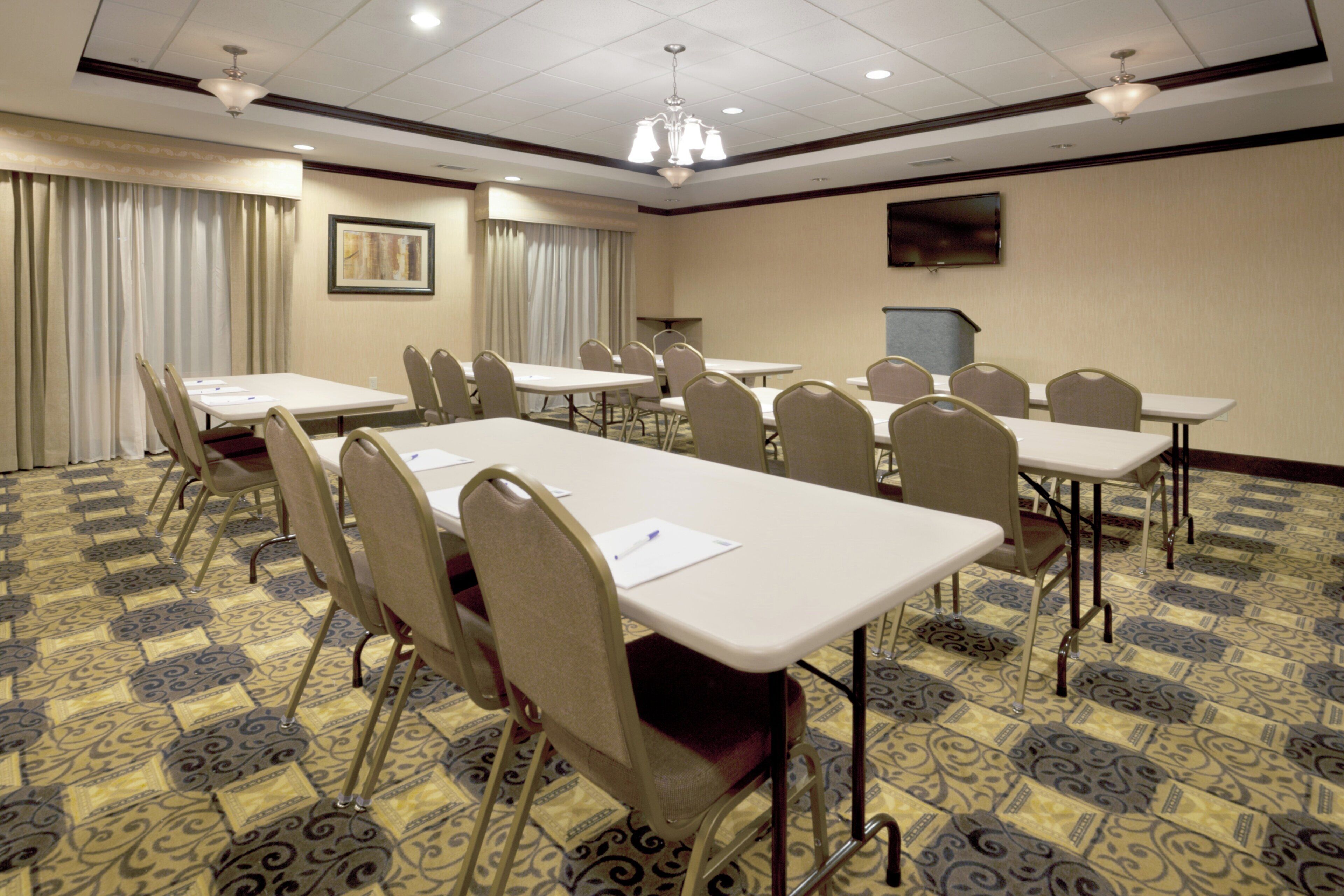 A conference room with multiple tables and chairs, a chandelier, and a painting on the wall.