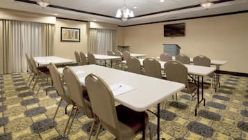 A conference room with multiple tables and chairs, a chandelier, and a painting on the wall.