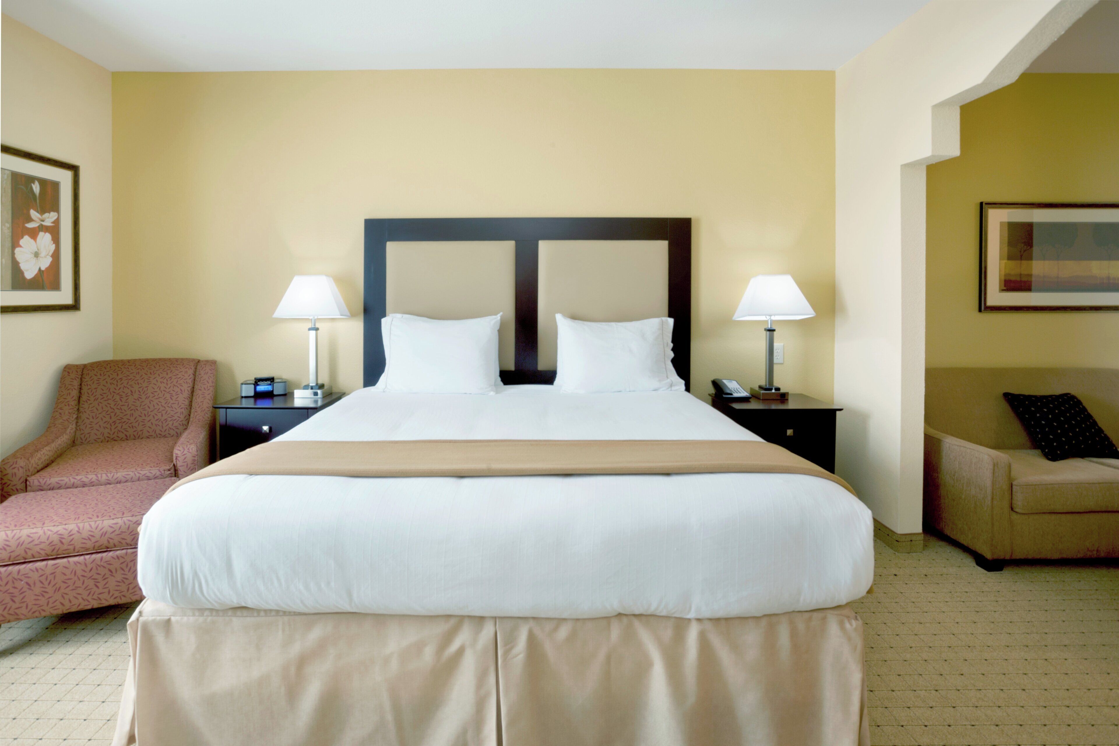 A hotel room with a large bed, two bedside tables, a chair, and a sofa.