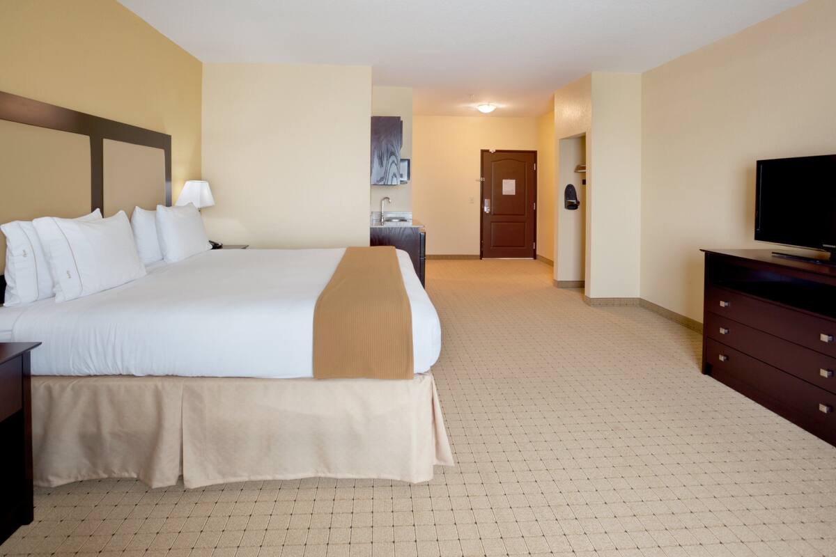 A hotel room with a large bed, a dresser, a television, and a bathroom visible in the background.