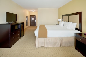 A hotel room with a bed, a TV on a dresser, a lamp, and a door leading to another room.