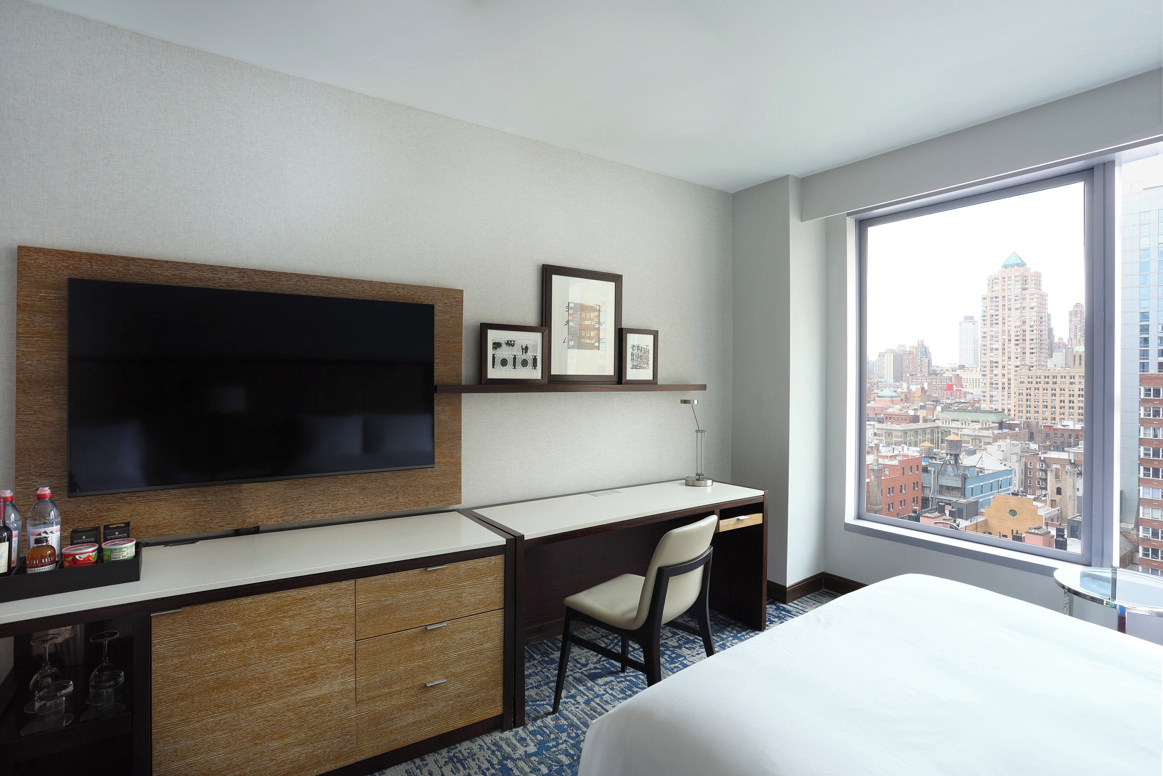 A hotel room with a large bed, a desk with a chair, a TV, and a city view.