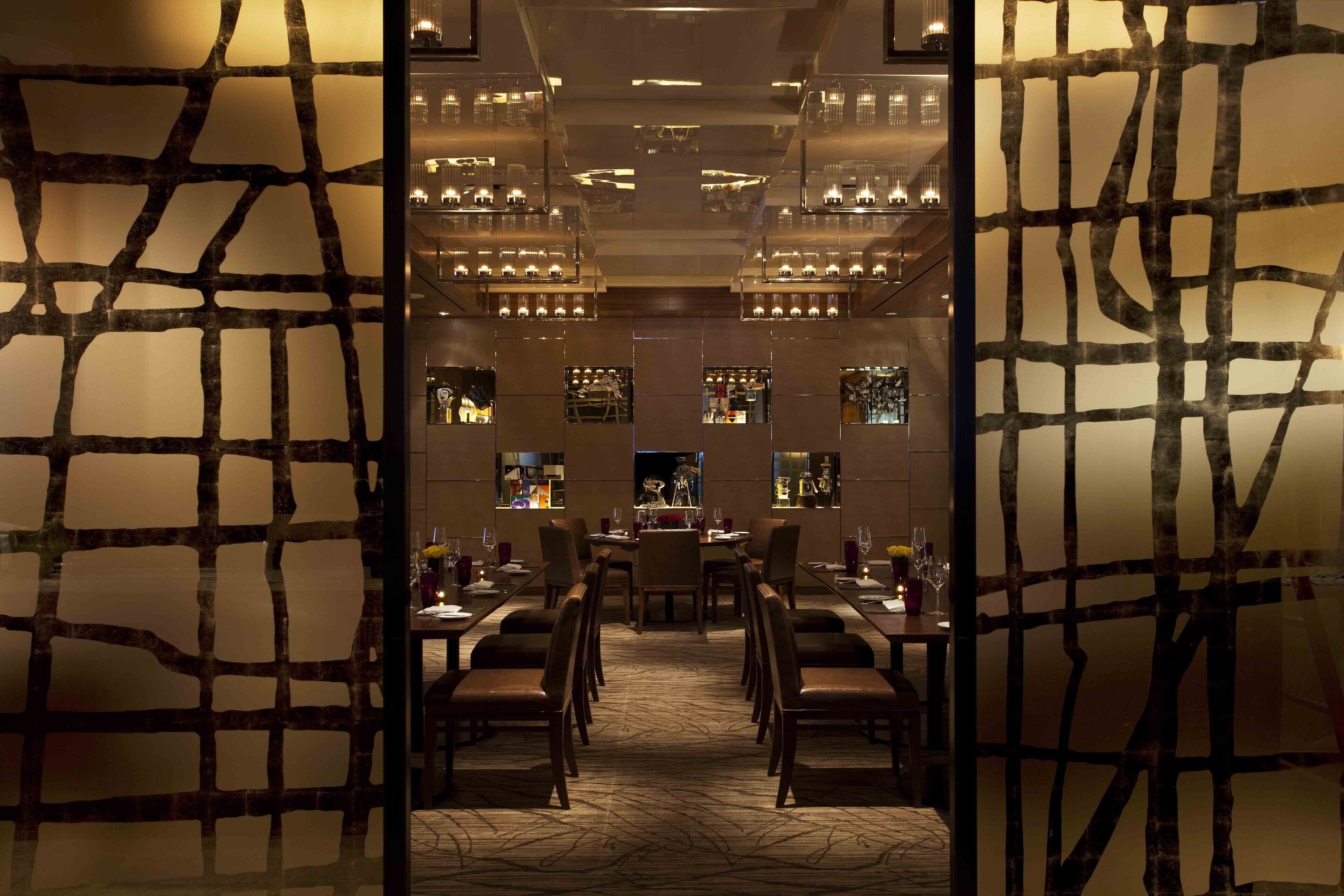 A hotel lobby with a central reception desk, multiple dining tables, and chairs arranged in the foreground.