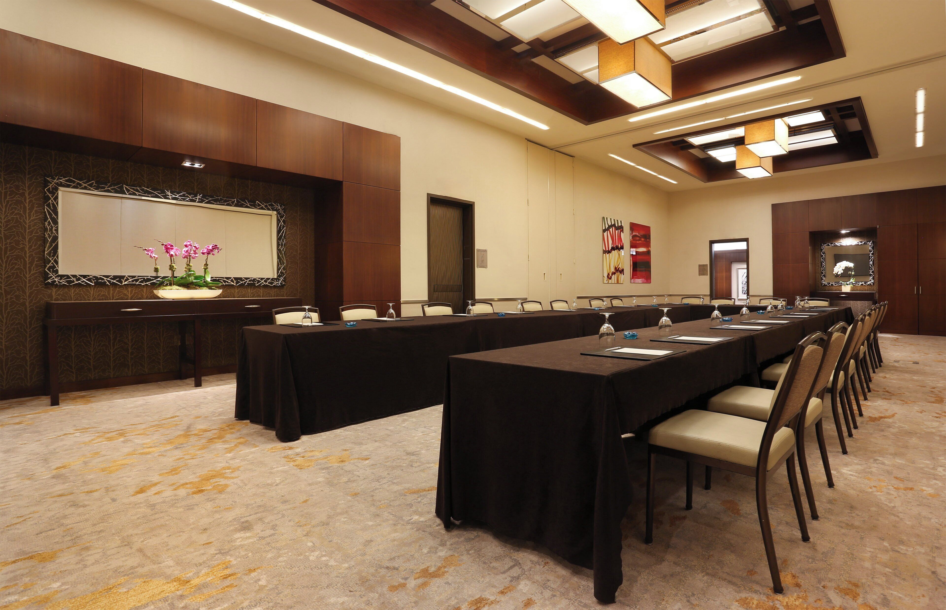Un salón de conferencias con una larga mesa, sillas, un espejo grande y un panel decorativo en la pared.