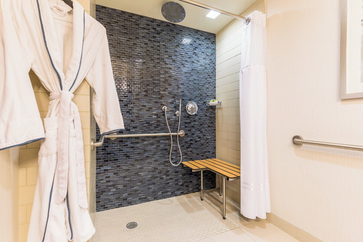 A modern bathroom with a shower, a bench, and a robe rack.