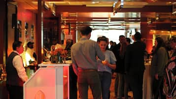 Un evento social concurrido en interiores, con gente de pie conversando, una recepción y una zona de bar.