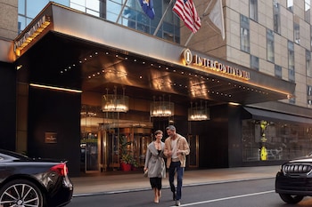 A modern hotel lobby with a fireplace, a stone wall, and a Christmas wreath. There are tables and chairs for guests to sit and relax. at InterContinental New York Times Square by IHG