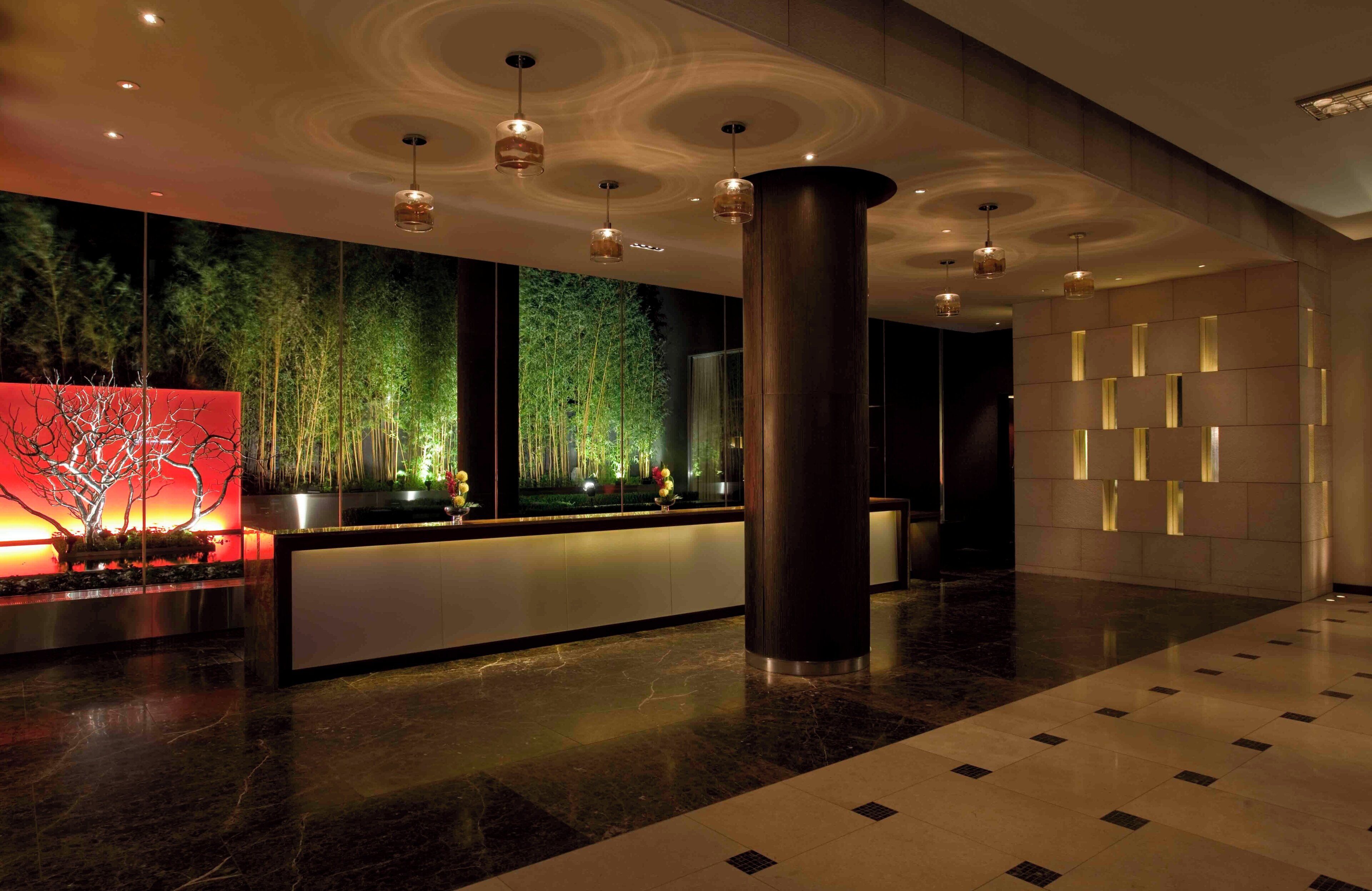 A modern lobby with a reception desk, a large pillar, and a wall with vertical light strips.