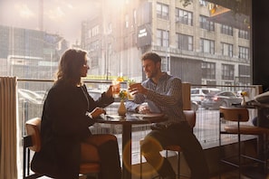 Two people sitting at a table with a city view, a glass of drink, and a vase with flowers.