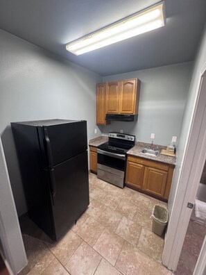 A compact kitchen with a black refrigerator, stainless steel oven, and wooden cabinets. - Palace Inn - Baytown I-10 (Baytown)