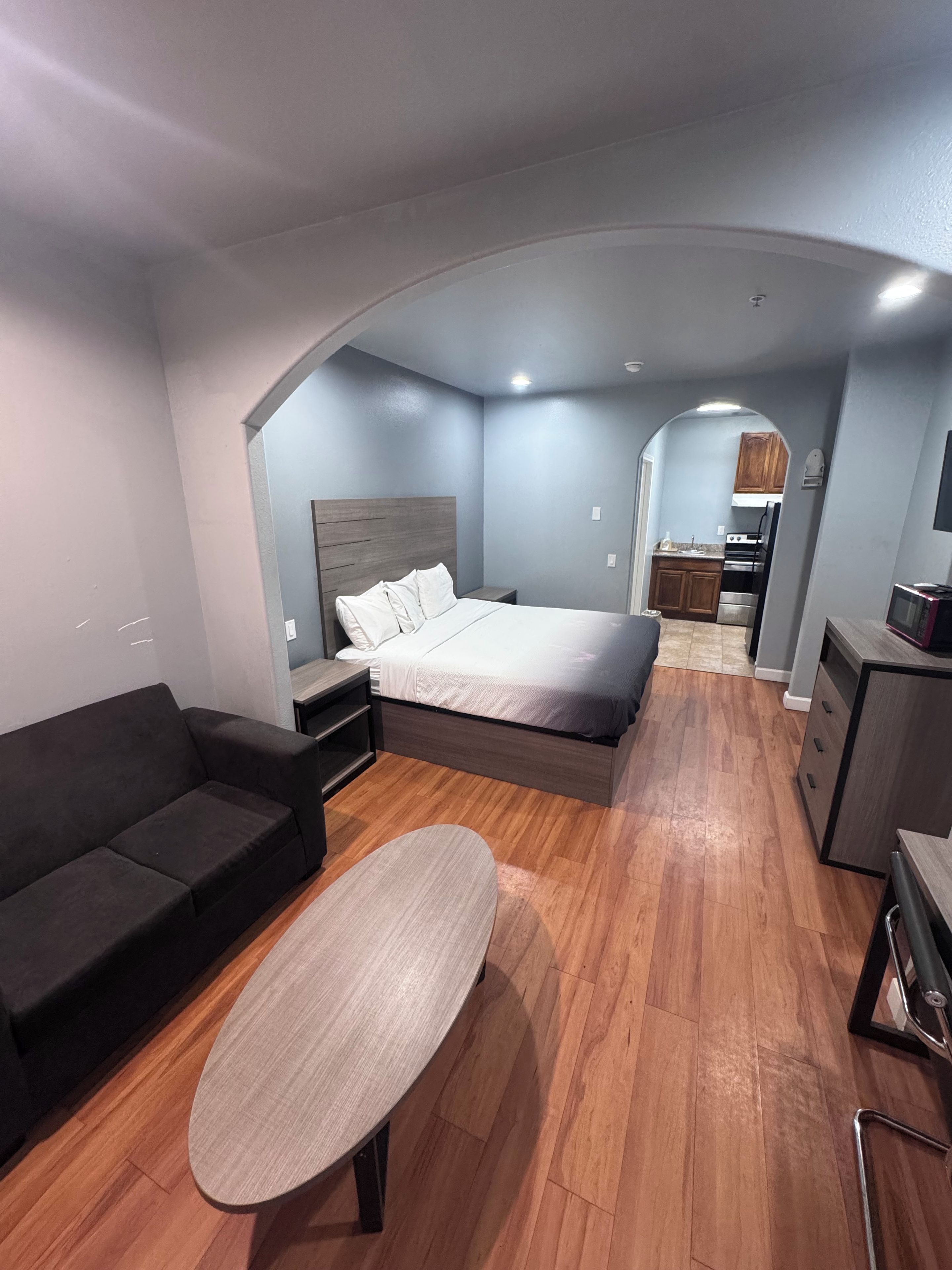 Un dormitorio moderno con una cama, un sofá, una mesita y un arco que da a una zona de cocina.