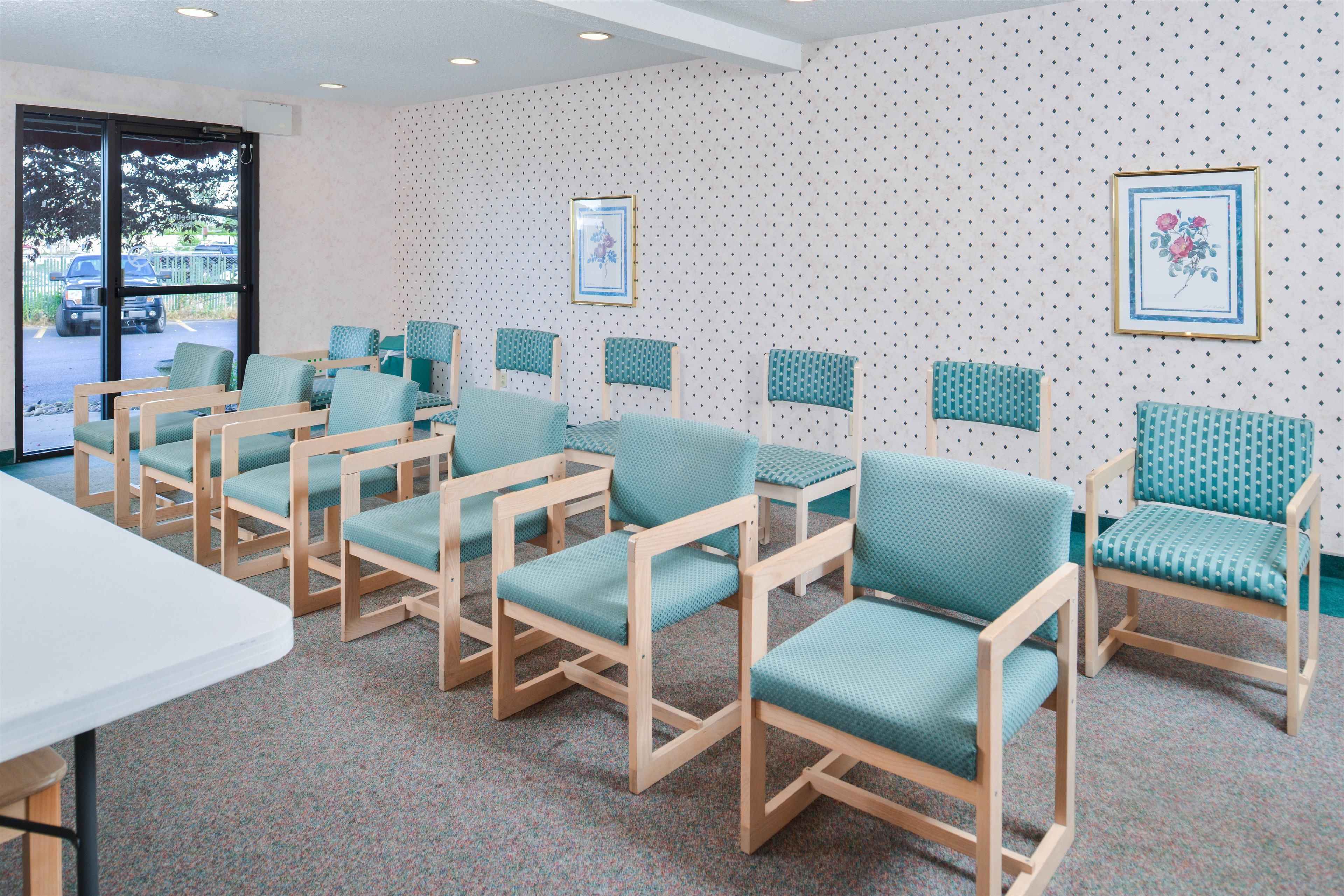 A seating area with teal chairs and a white table, a patterned wall, and a door leading outside.
