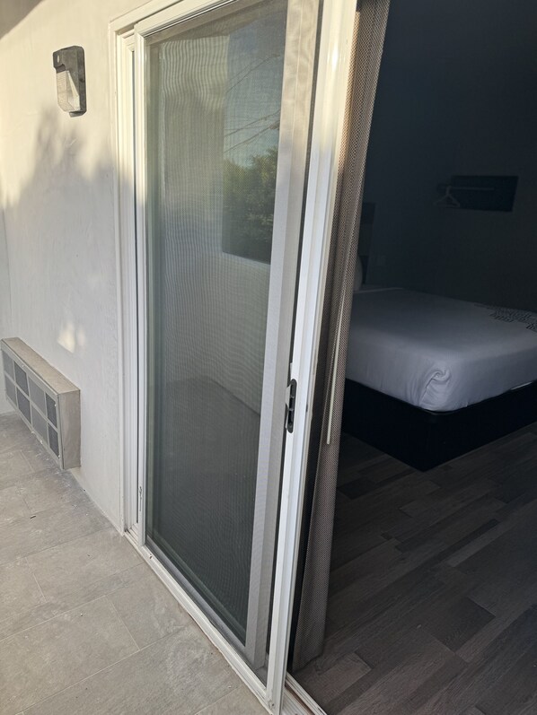 A room with a sliding glass door leading to a balcony, a bed with a mattress and pillows, and a small window. - Surfside Inn Redondo Beach (Redondo Beach)