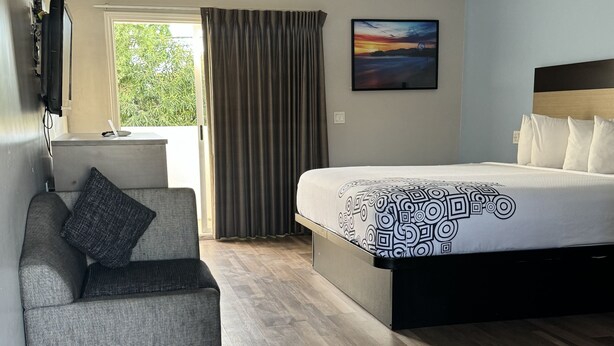 A modern hotel room with a bed, a sofa, a TV, and a window with curtains. - Surfside Inn Redondo Beach (Redondo Beach)