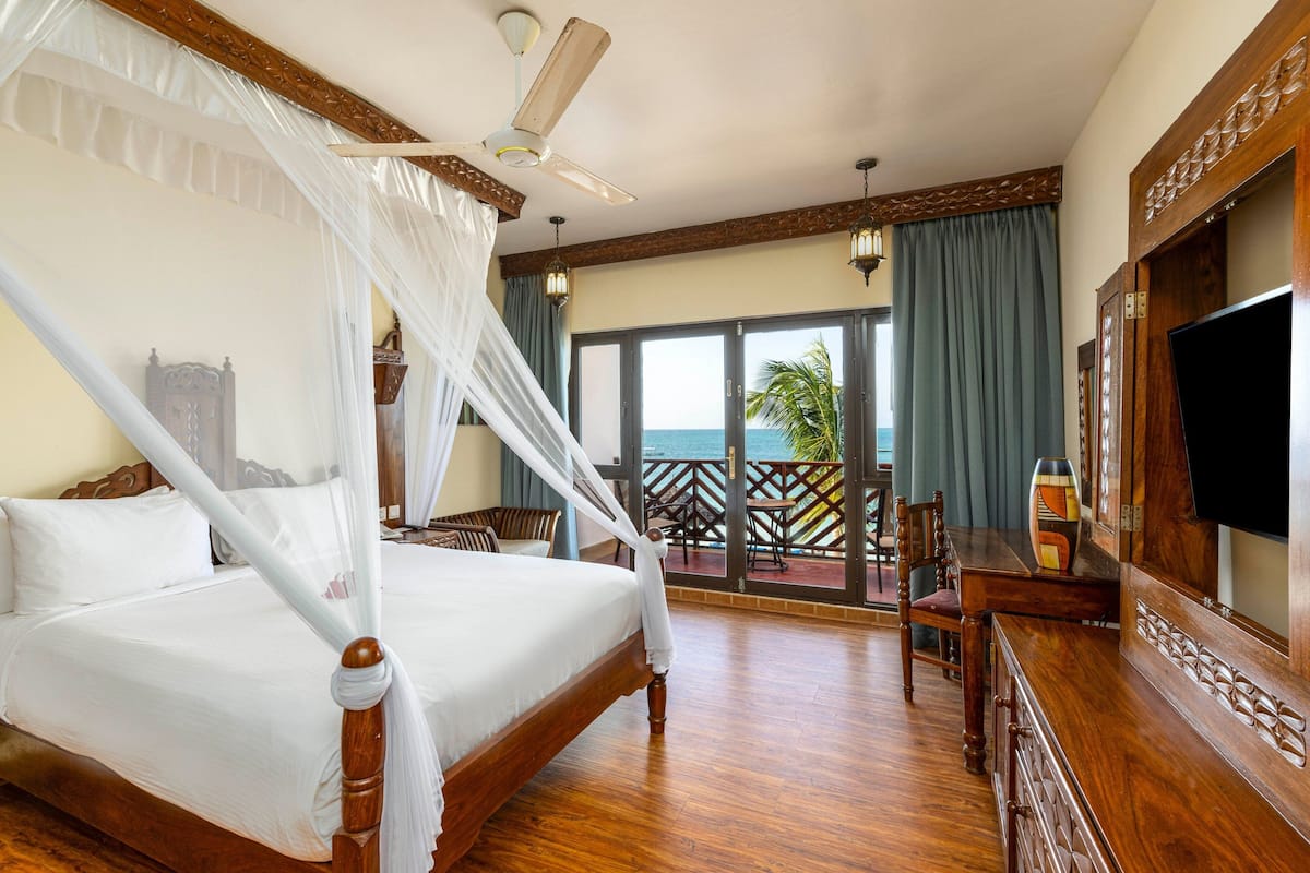 A four-poster bed with a canopy, a television, and a balcony with a view of the ocean.