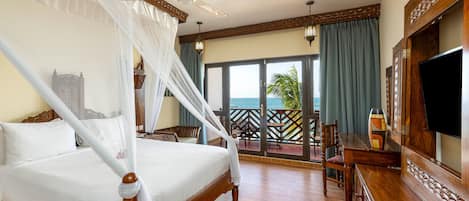 A four-poster bed with a canopy, a television, and a balcony with a view of the ocean.