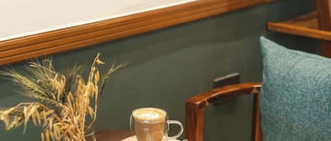 Un comedor con una mesa de madera, una taza de café, un plato de croissants y un florero con plantas secas.