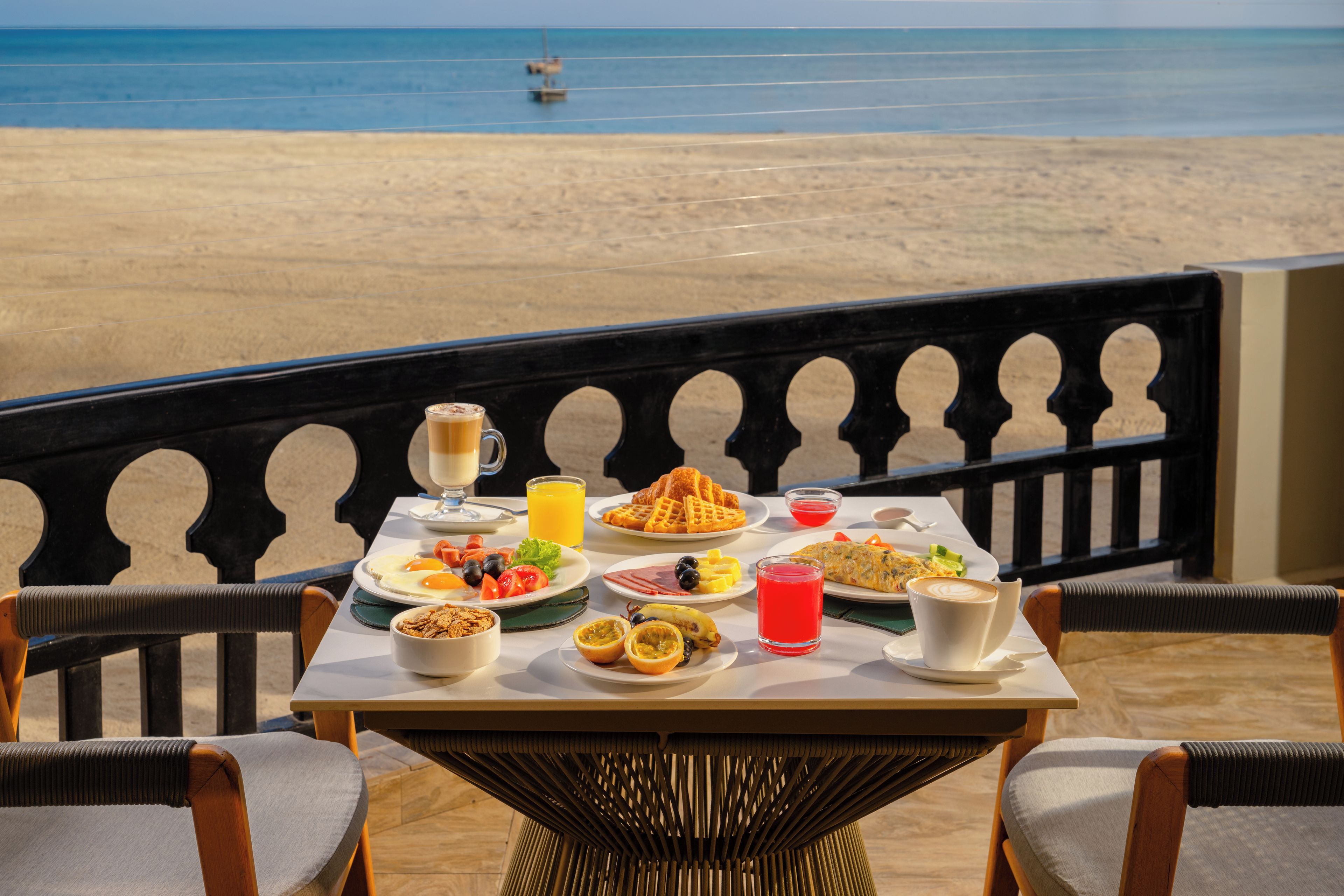 A table set with breakfast items, including waffles, eggs, and fruit, overlooking a beach.