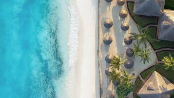An aerial view of a beach with white sand, clear blue water, and thatched-roof structures.