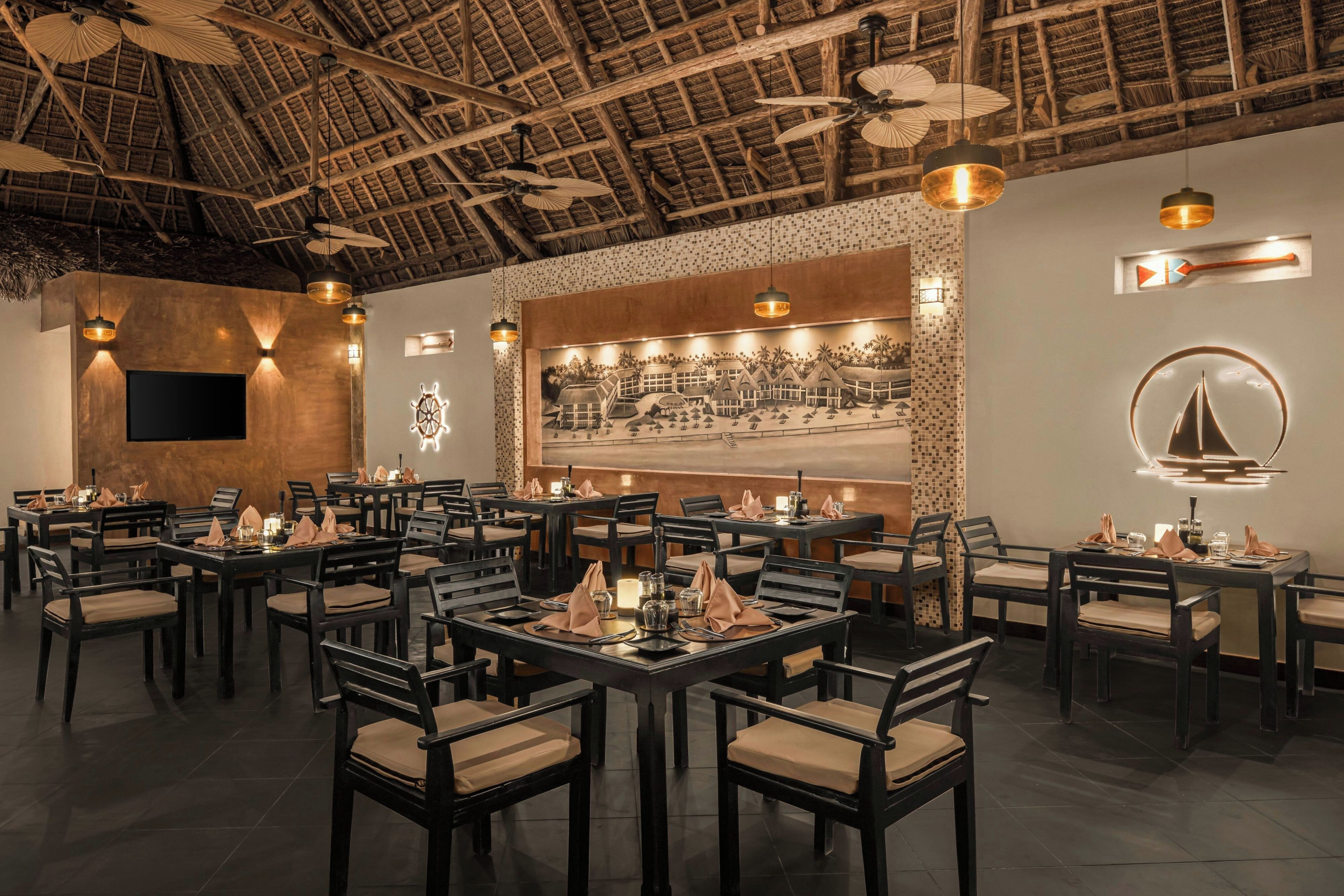 Un ristorante con diversi tavoli e sedie, un grande affresco al muro e una ventola a soffitto.