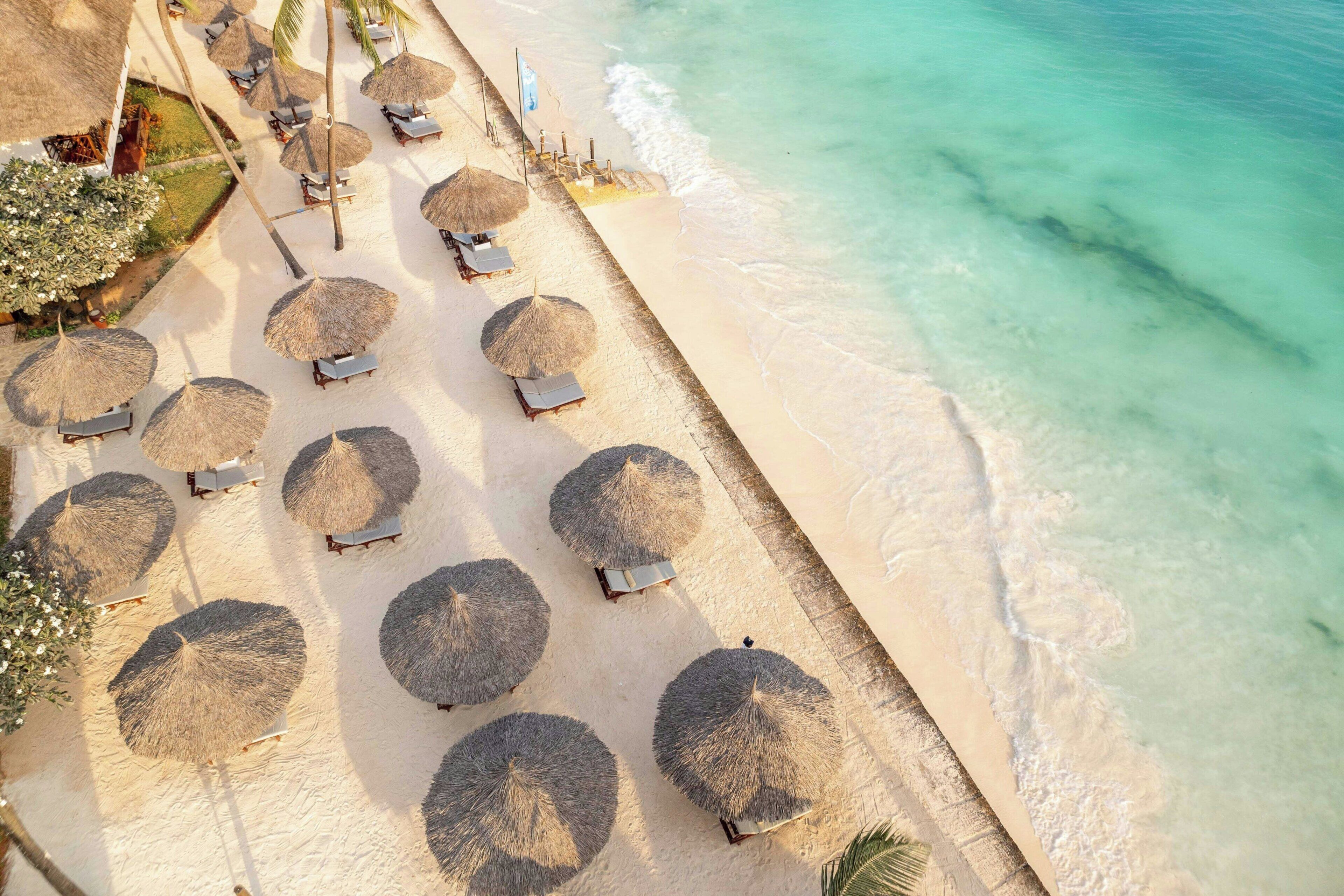 An aerial view of a beach with rows of sun loungers and thatched umbrellas.
