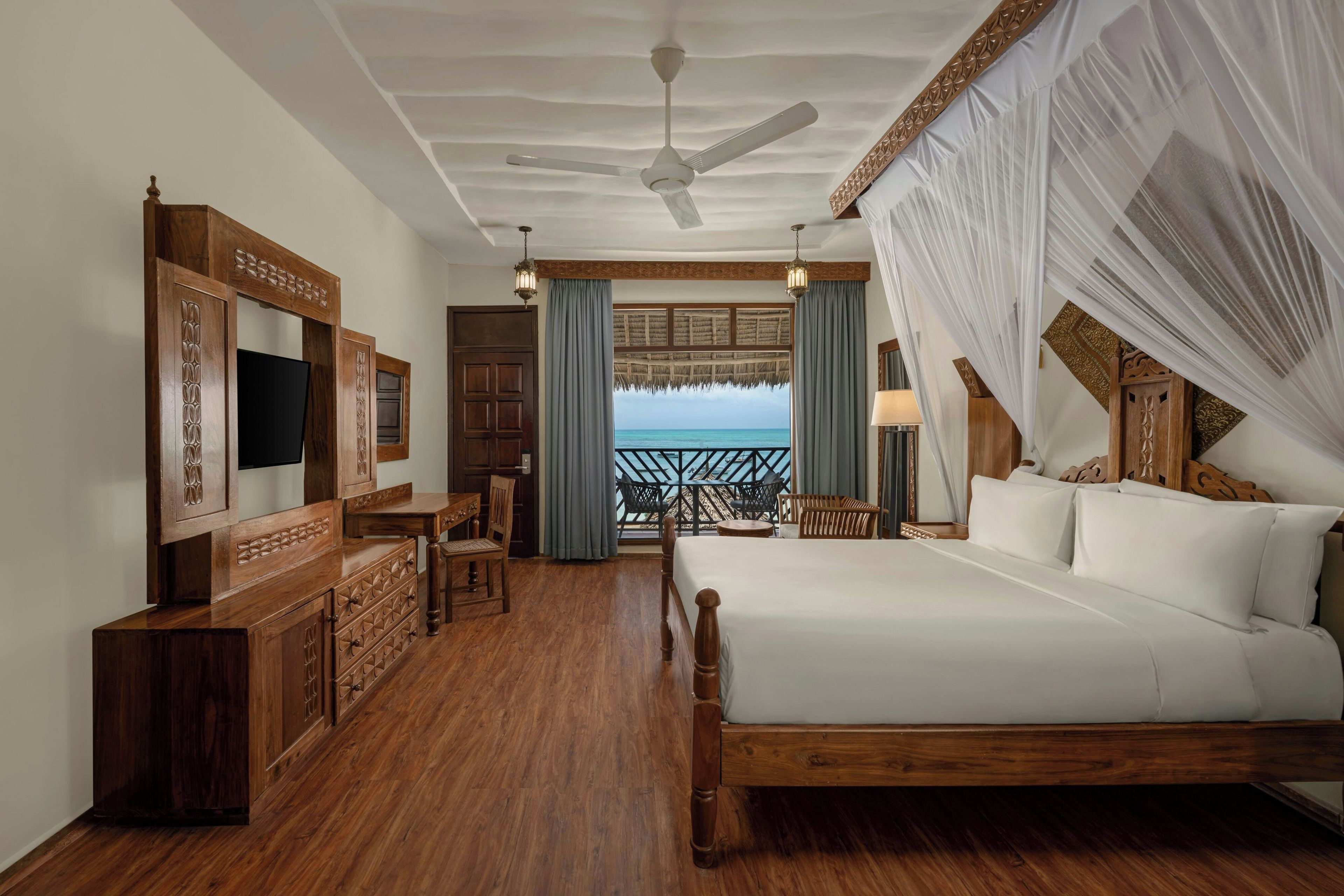A hotel room with a bed, a TV, a desk, and a balcony with a view of the sea.