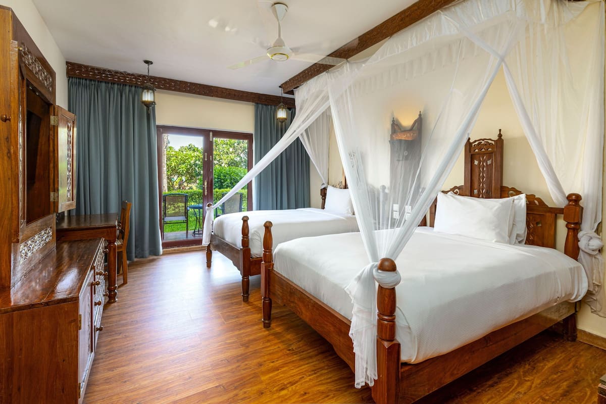 A bedroom with two wooden beds, a wooden dresser, a ceiling fan, and a view of the outdoors through a glass door.