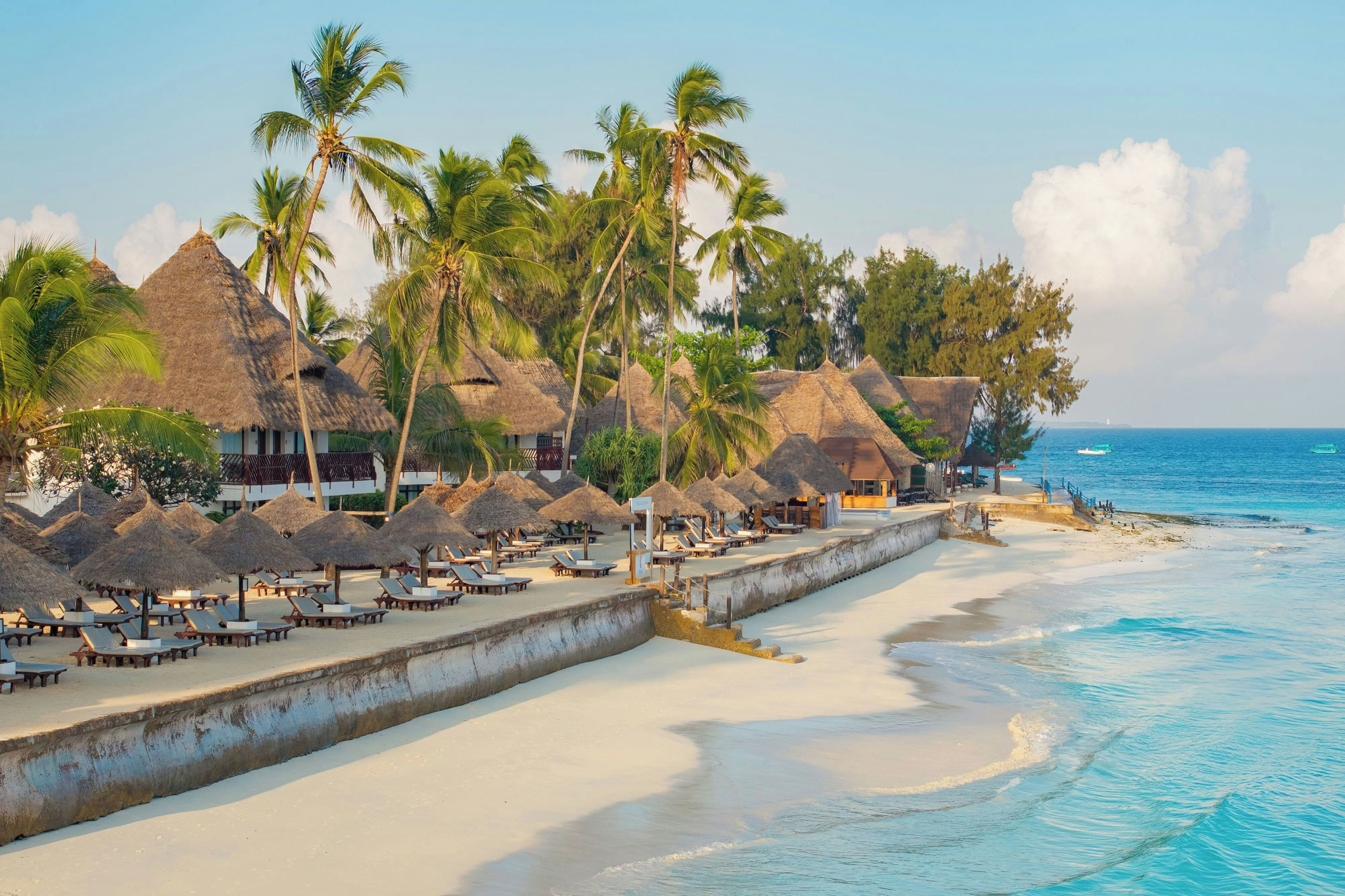 A beach resort with thatched-roof huts, sun loungers, and a sandy shoreline.