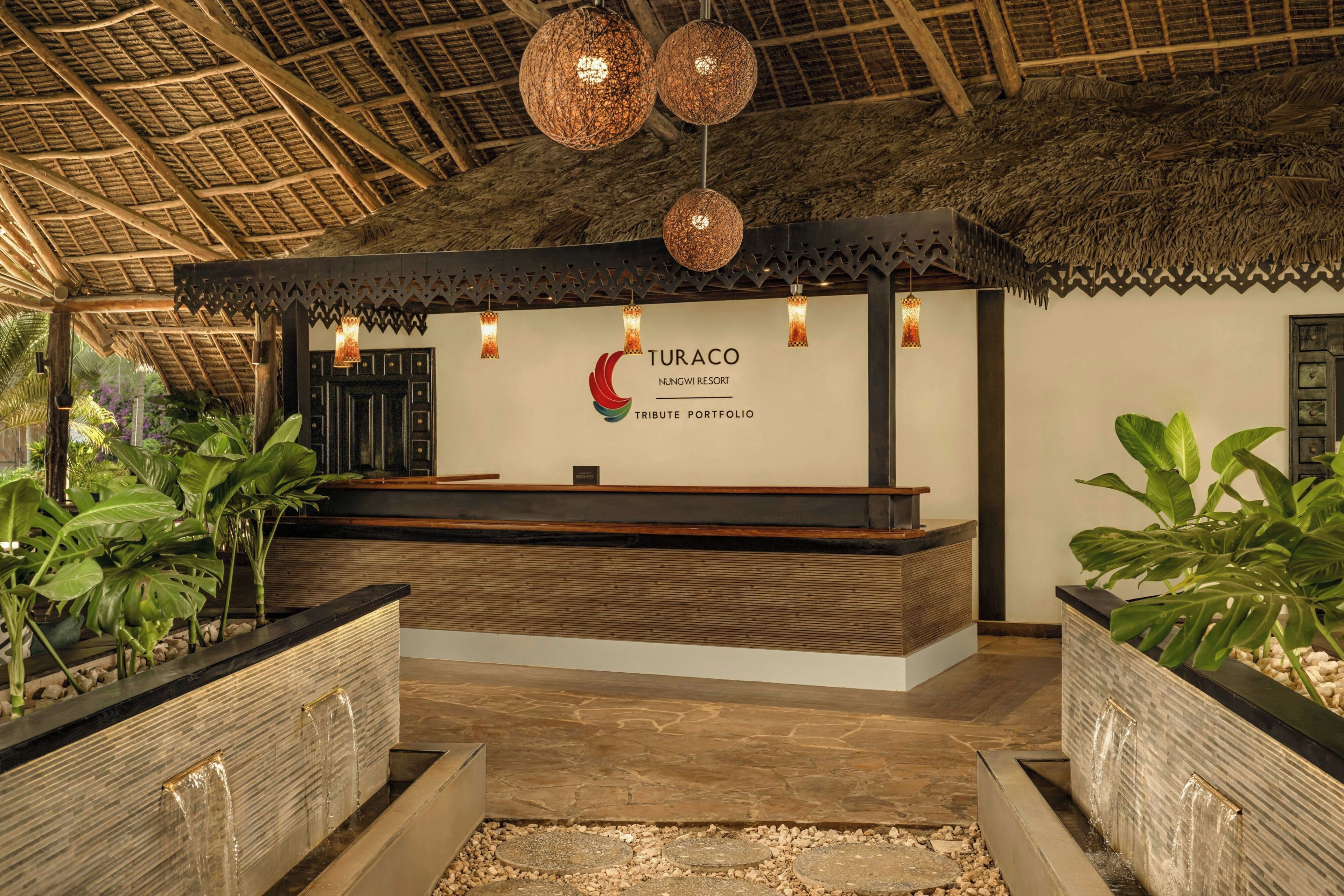 Zona de recepción con techo de paja, mostrador de recepción e iluminación decorativa colgante.