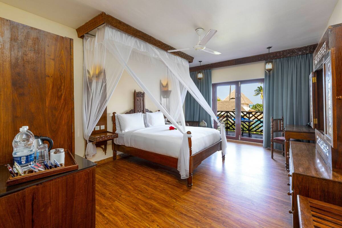 A spacious bedroom with a wooden bed, a nightstand, a desk, and a balcony with a view.