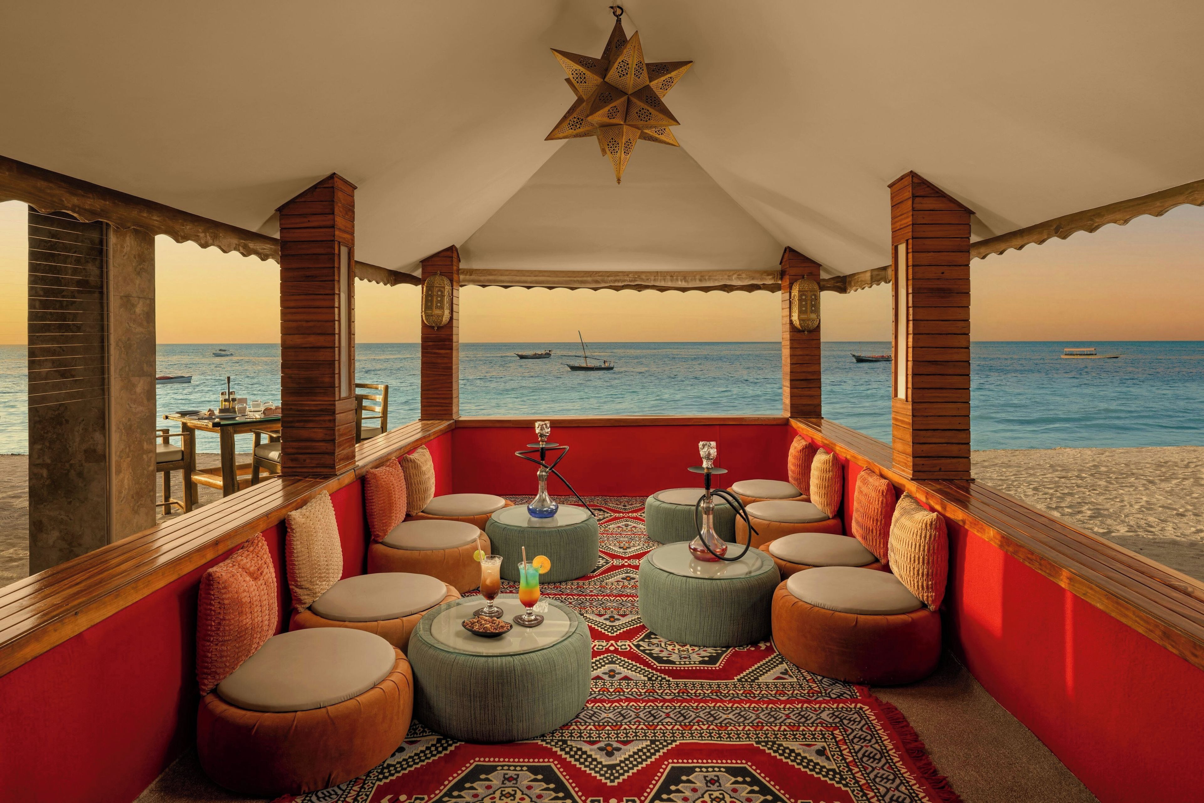 A beachside lounge with wooden pillars, round ottomans, and a star-shaped hanging light fixture.