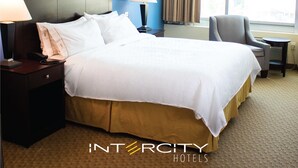 A hotel room with a large bed, two bedside lamps, a chair, and a window with curtains.