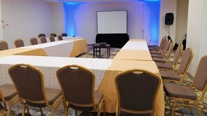 A conference room with a long table, chairs, a projector screen, and a speaker.