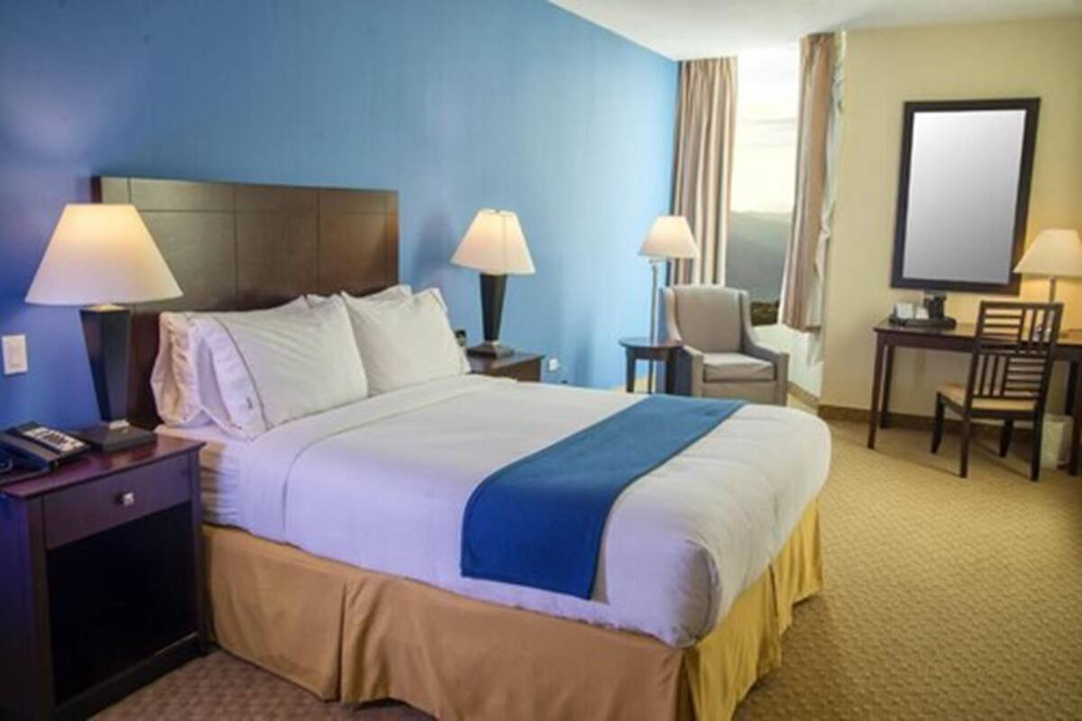 Une chambre d’hôtel avec un grand lit, deux tables de chevet avec des lampes, un bureau avec une chaise et un grand miroir au mur.
