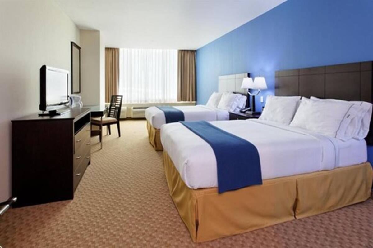 Une chambre d’hôtel avec deux lits, un bureau avec une télévision, une chaise et une fenêtre avec des rideaux.