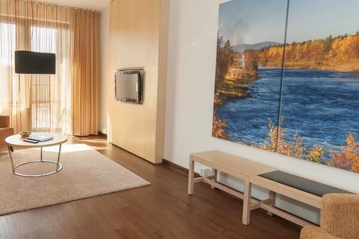 Una sala de estar moderna con un sofá, un sillón, una mesa de centro y un cuadro de un paisaje fluvial.