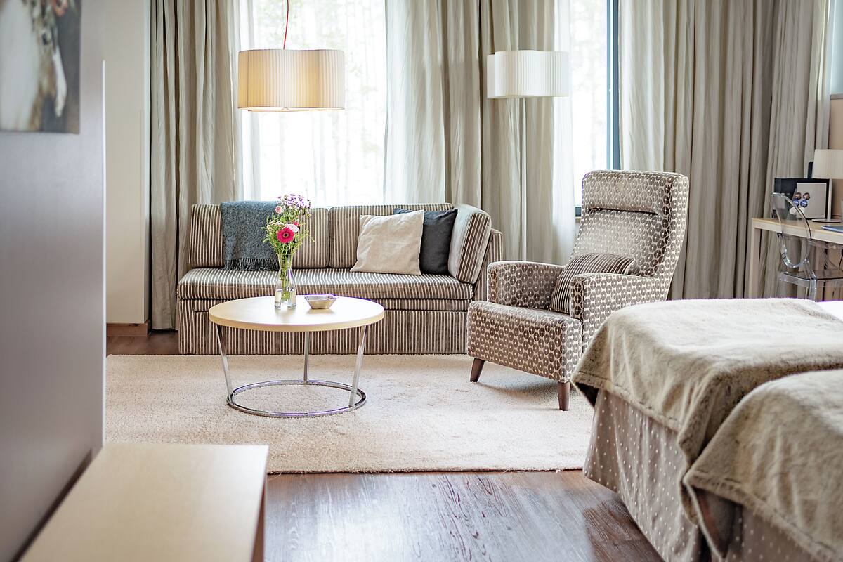 Una habitación de hotel acogedora con un sofá a rayas, un sillón estampado, una mesa de centro redonda y una cama con colcha de lunares.