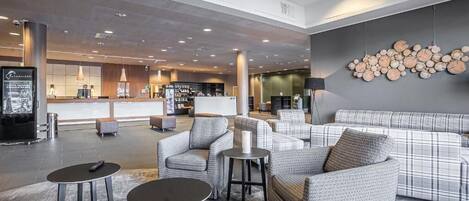 A modern lobby with a sofa, armchairs, and a coffee table. There is a reception desk in the background.