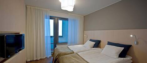 Habitación de hotel con dos camas, un televisor, una lámpara en el techo y vistas al exterior a través de un ventanal.