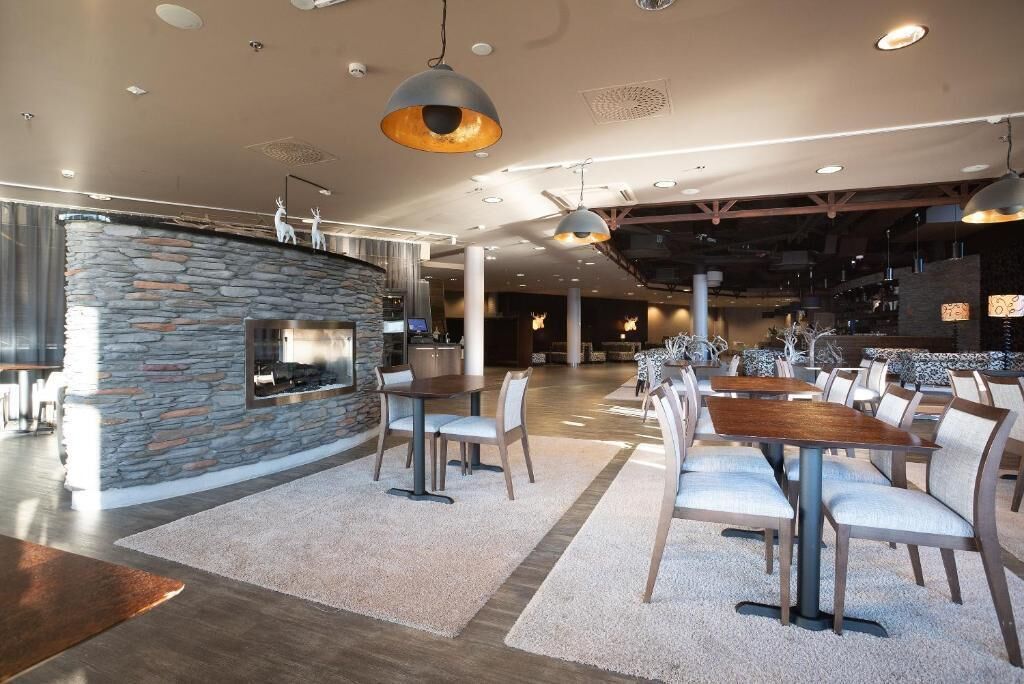 Un restaurant spacieux avec un mur en pierre, de nombreuses tables et un éclairage moderne suspendu au plafond.