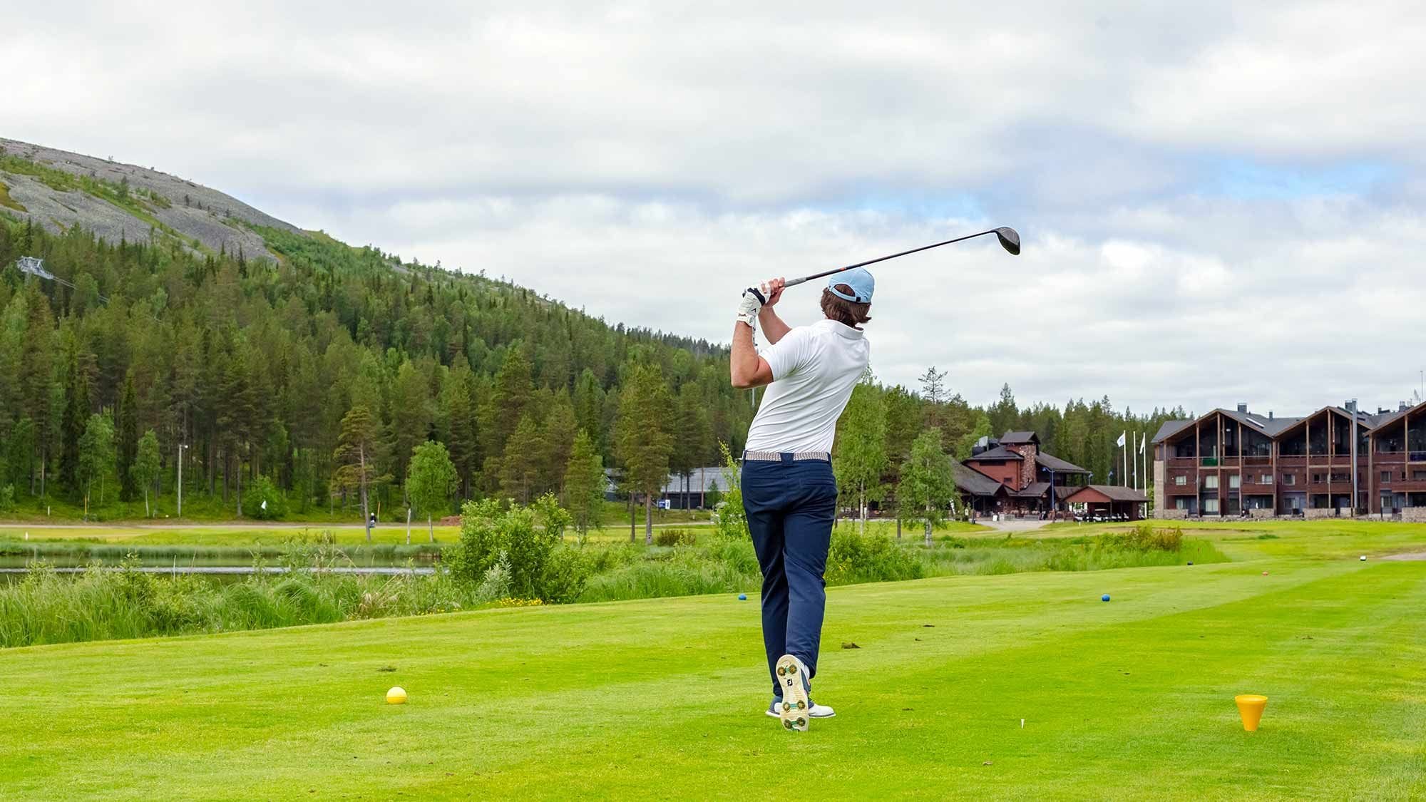 A golf course with a player in mid-swing, a pond, and lodge buildings in the background.