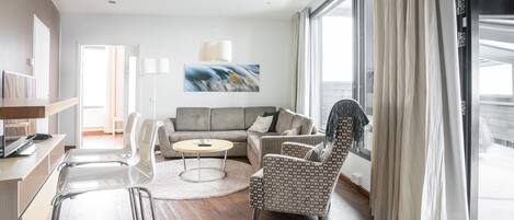 Ein modernes Wohnzimmer mit einer Couch, Sesseln, einem Couchtisch und einem großen Fenster mit Vorhängen.