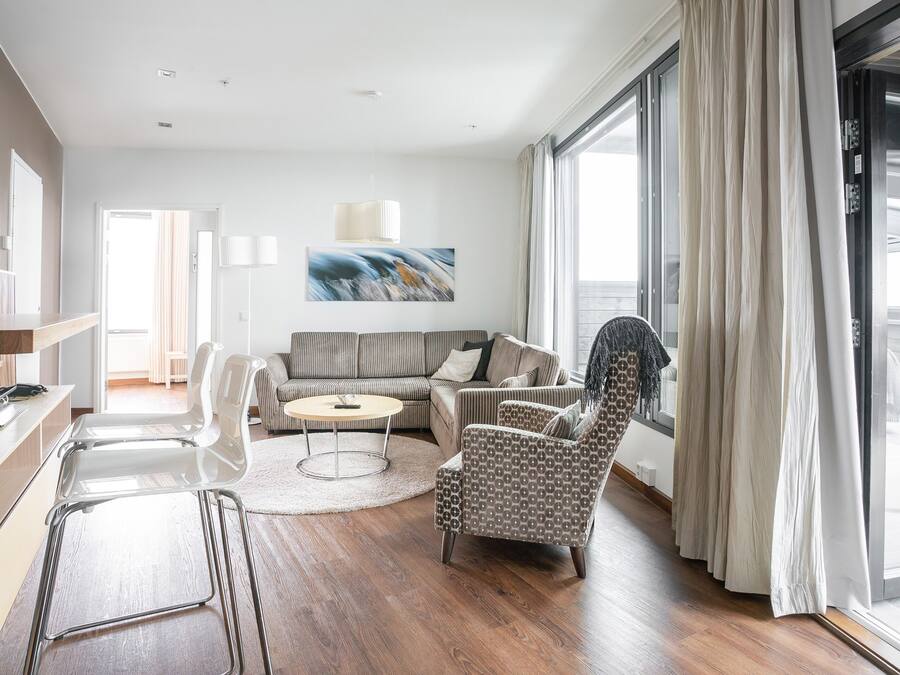 A modern living room with a sofa, armchairs, a coffee table, and a large window with curtains.